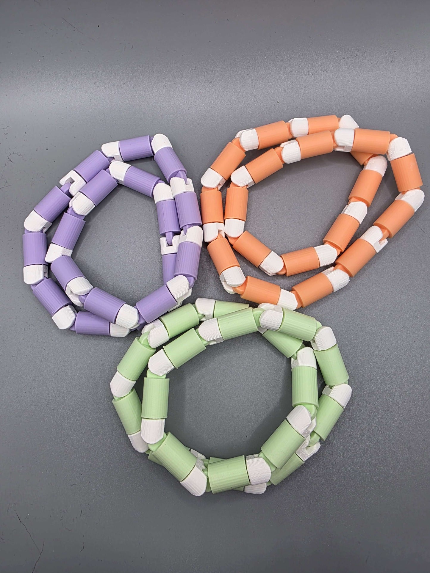 sensit twist by 3dFidgets - Colorful tactile fidget toys in purple, orange, and green arranged on a gray background.
