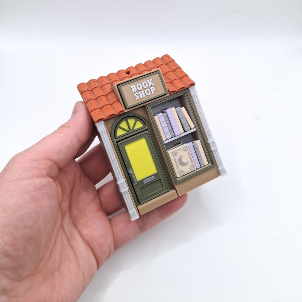 Miniature model of a bookshop held in a hand against a white background