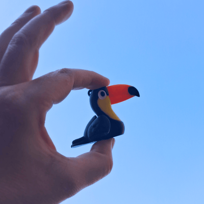 Hand holding a small figurine of a toucan against a clear blue sky