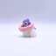 Toy figure of a pigeon with a purple head and pink donut-like body on a light gray background