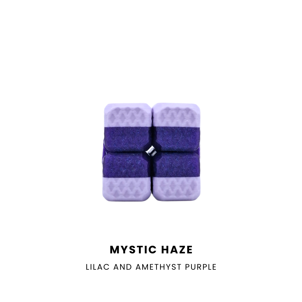 A 4-piece fidget cube with a textured lilac outer shell and dark purple textured inner sections, featuring a small black and white logo in the center. Below the product, the text reads 'MYSTIC HAZE' and 'LILAC AND AMETHYST PURPLE' on a solid white background.