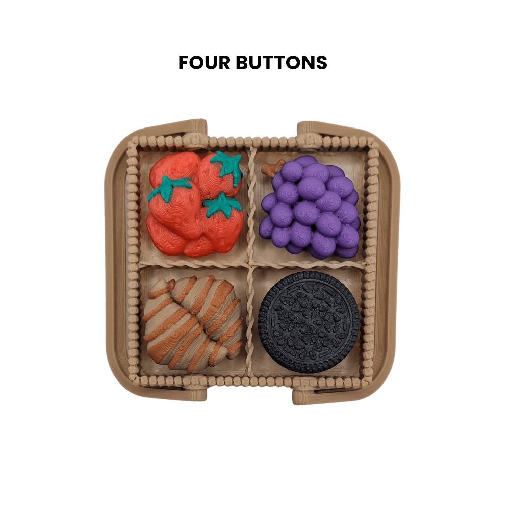 Four clicker buttons in a compartmentalized container with a strawberry's, grapes, cookie, and round button.