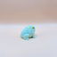 Small green frog figurine on a beige background